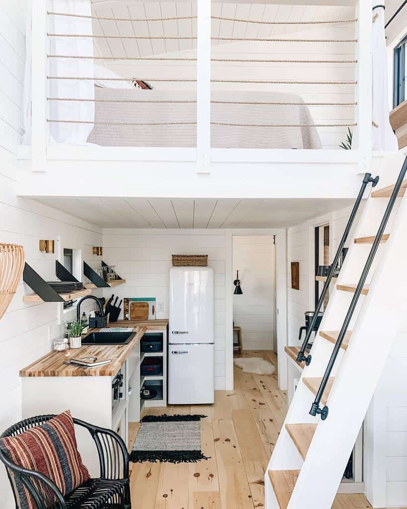 Bright tiny home with a lofted bedroom, compact kitchen, and wooden accents. A ladder with black railings leads to the cozy sleeping area.