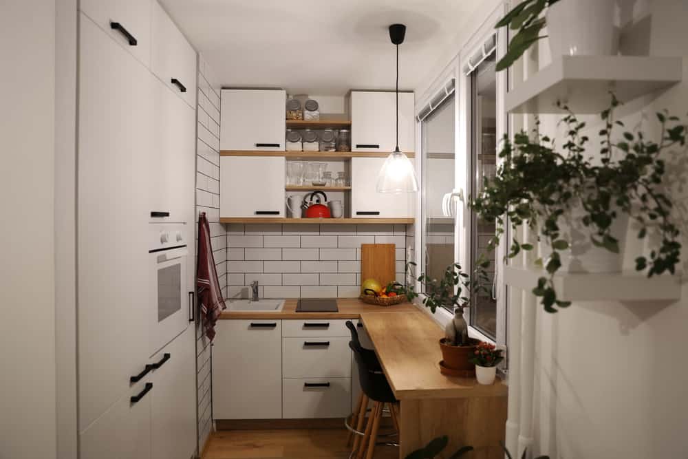 Modern tiny house kitchen with white cabinets, subway tile backsplash, and wooden countertops. Open shelves and plants add warmth and charm.