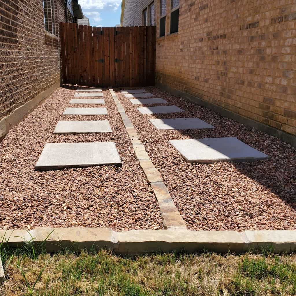 A neatly arranged gravel path with concrete stepping stones leads to a wooden gate between two brick walls