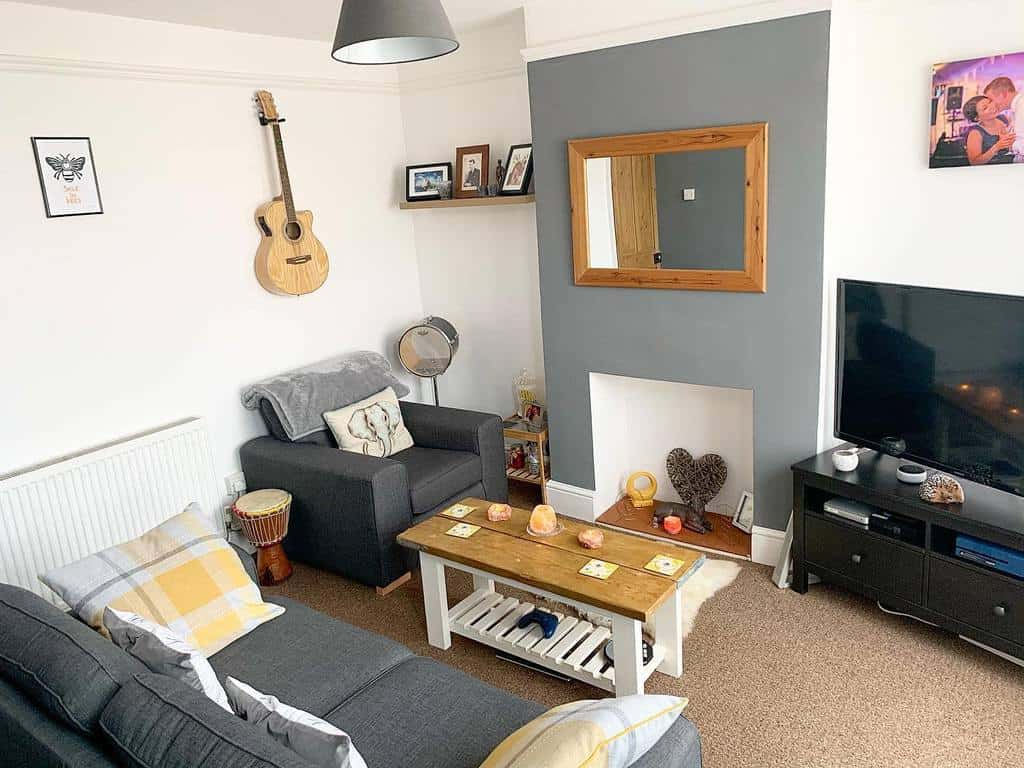 Cozy living room with a wall-mounted guitar, a djembe drum, a fireplace, neutral-toned seating, and warm decorative accents