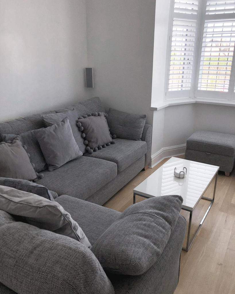 Modern glass-top coffee table with a sleek chrome frame, set in a minimalist living room with a grey sofa and neutral decor