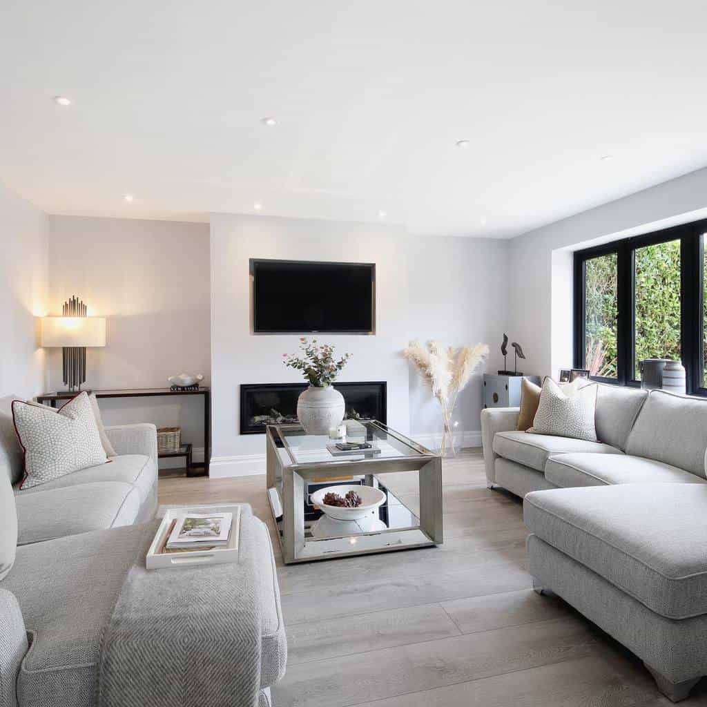 Modern mirrored coffee table with a geometric frame, styled with a vase, books, and decor, set in a sleek, neutral-toned living room