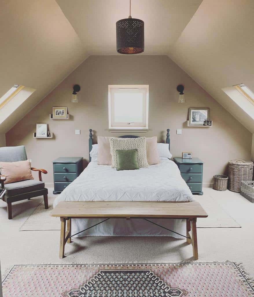 Cozy attic bedroom designed for small spaces, featuring a bed, pillows, side tables, a chair, bench, and slanted ceilings with skylights.