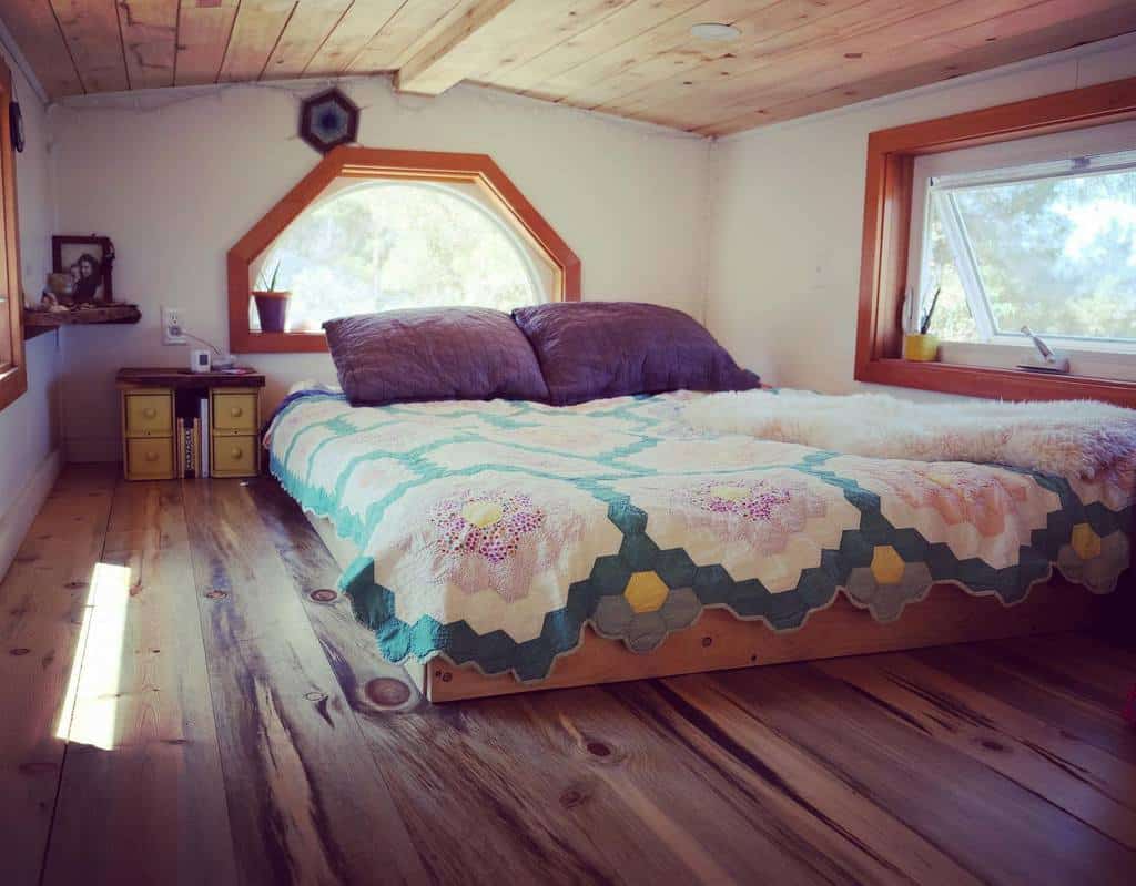 Cozy loft bedroom with a colorful quilted bed, plush pillows, and rustic wooden floors. Ideal for small spaces with its ample natural light.