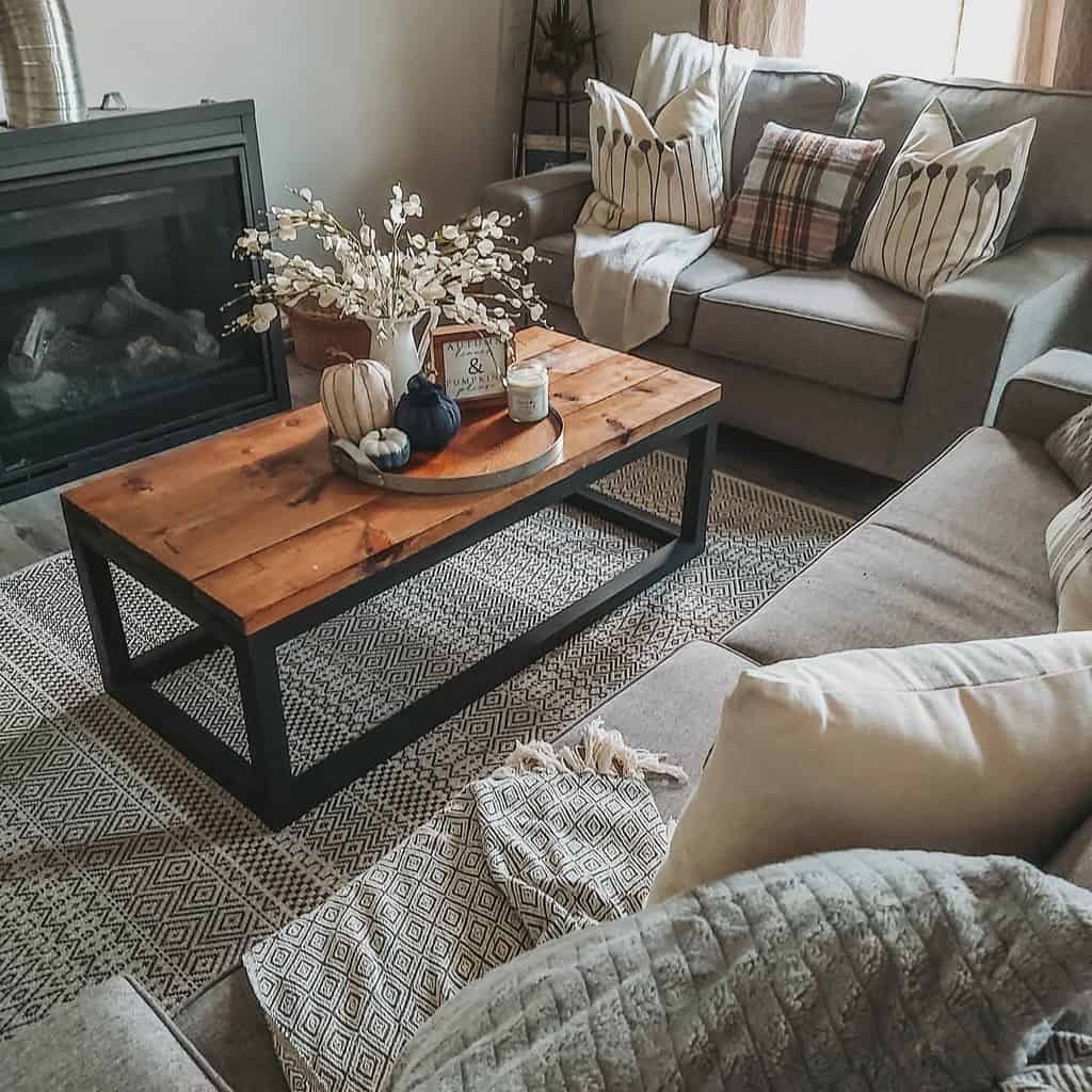 Rustic wood and metal coffee table styled with fall decor, a vase, and candles, set in a cozy living room with neutral tones and a fireplace