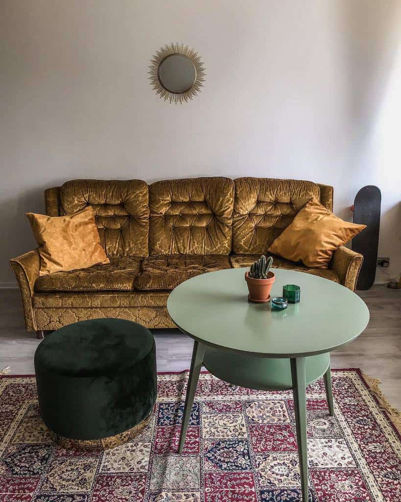 Vintage living room with a brown sofa, gold pillows, green round table, cactus, green pouf, patterned rug, and sunburst mirror