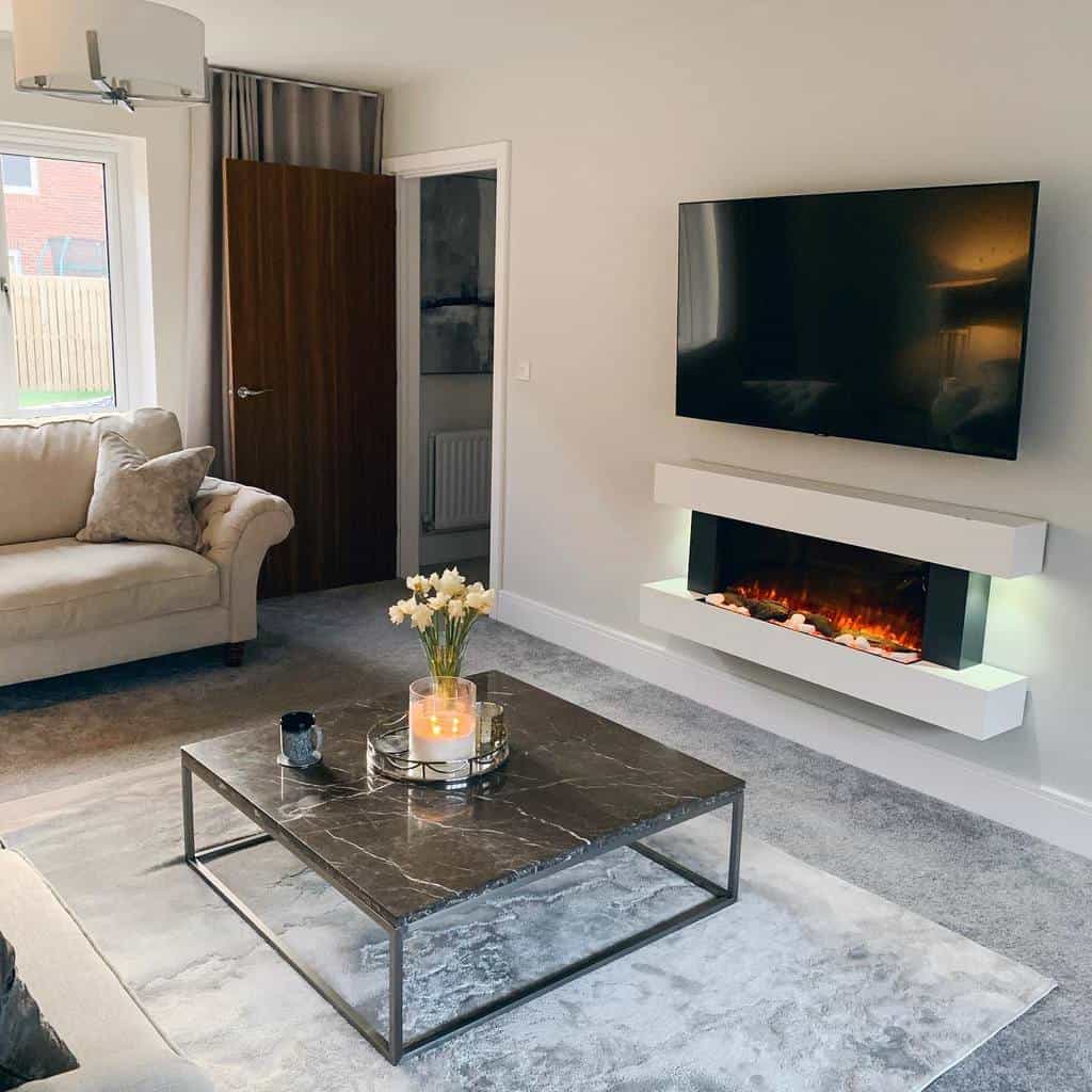 Modern living room with a wall-mounted TV, electric fireplace, beige sofa, and a marble coffee table with flowers and candles