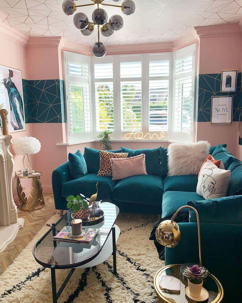 Modern oval glass coffee table with a black metal frame, styled with a tray, candle, and magazines, set in a chic pink and teal living room