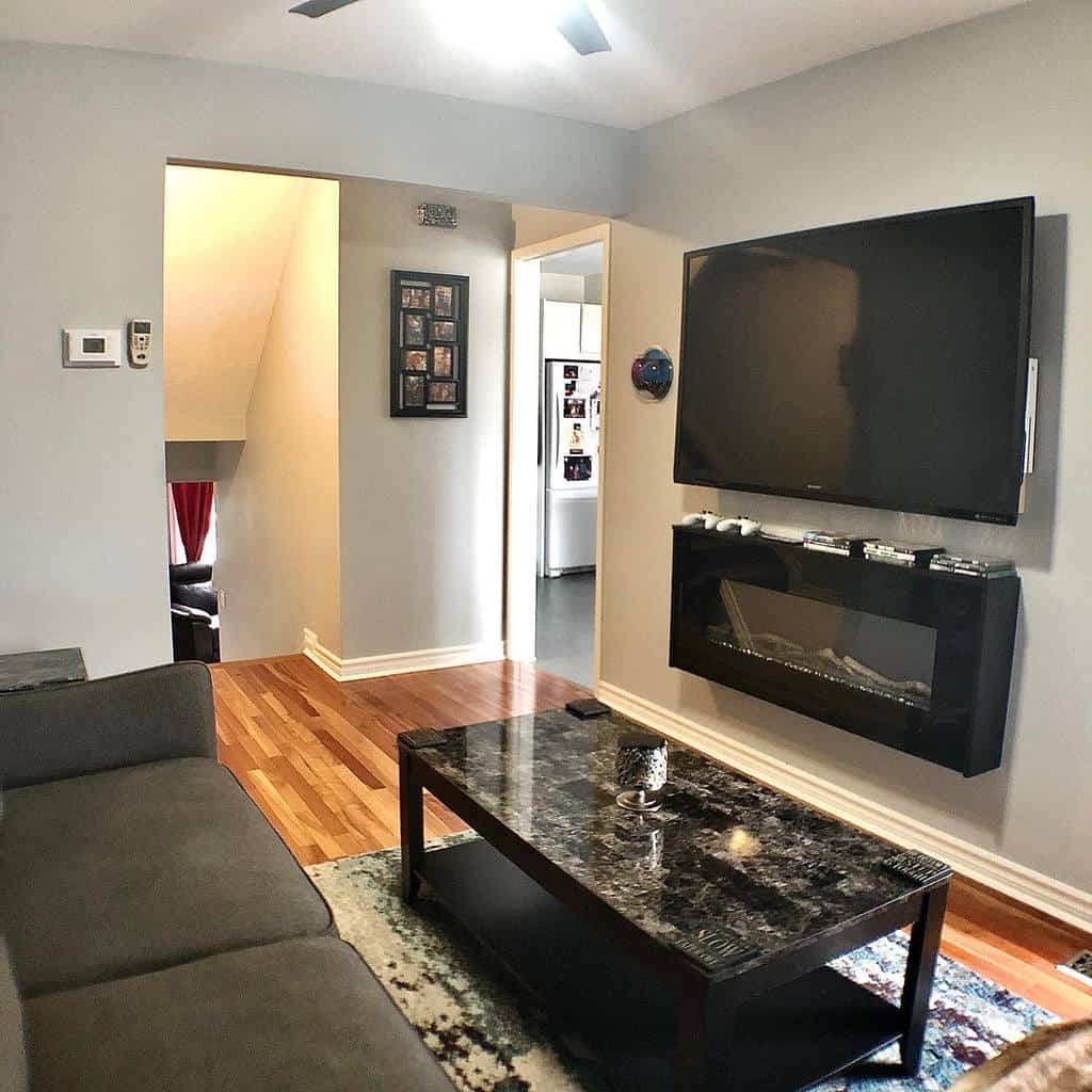 Modern living room with a wall-mounted TV, electric fireplace, gray sofa, and a marble-topped coffee table on a patterned rug