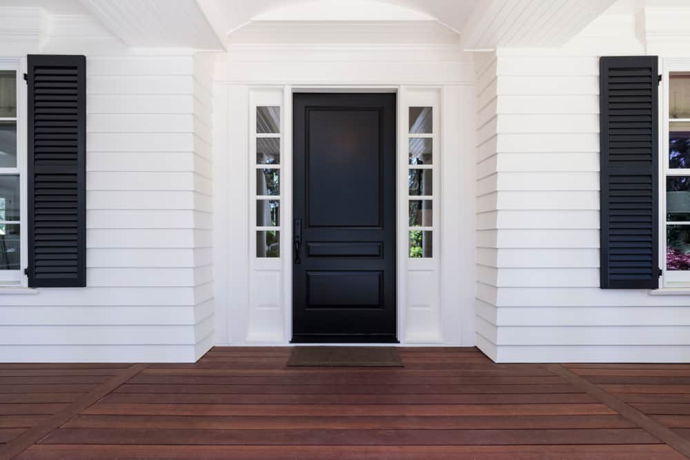 White house entrance with a black door, flanked by sidelights and black shutters