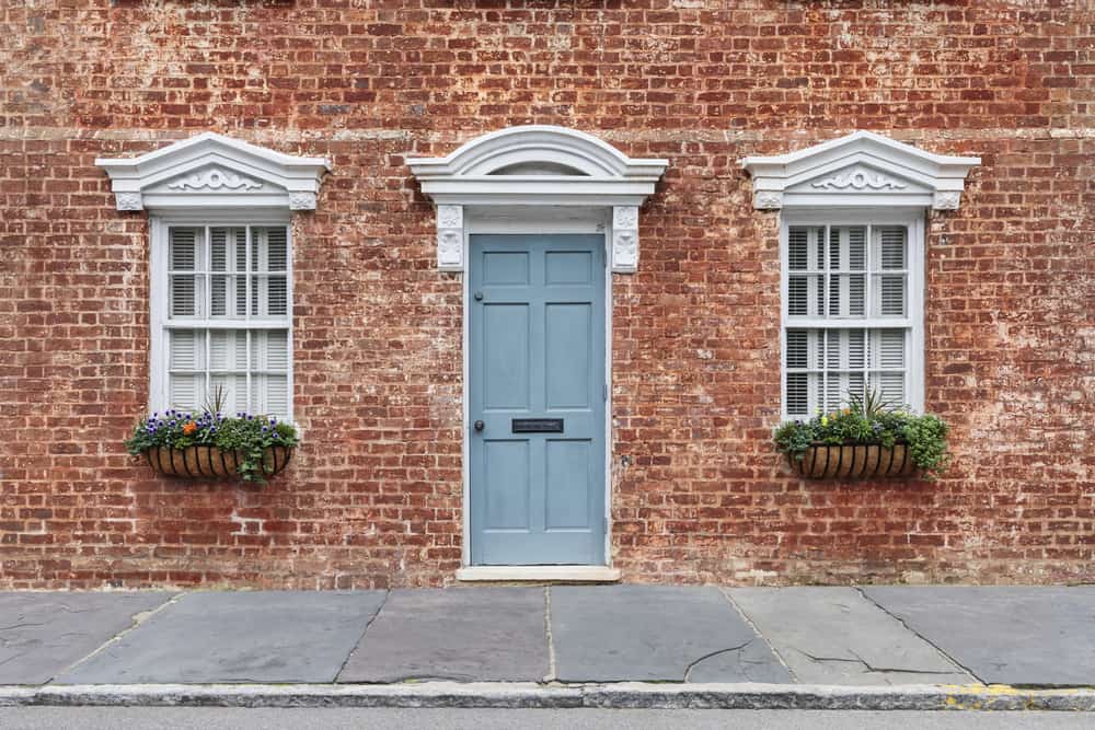 Red brick wall with a blue door, white-framed windows, and flower boxes, stone pavement in front