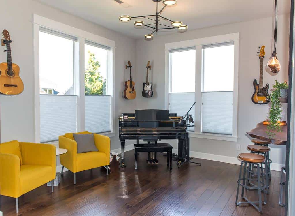 Bright modern music room with a grand piano, wall-mounted guitars, yellow accent chairs, stylish lighting, and a cozy bar area