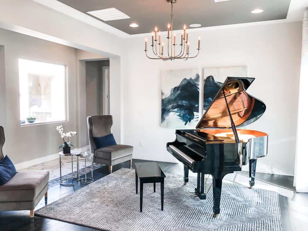 Elegant music room with a grand piano, modern chandelier, abstract artwork, cozy seating, and a sophisticated neutral color palette