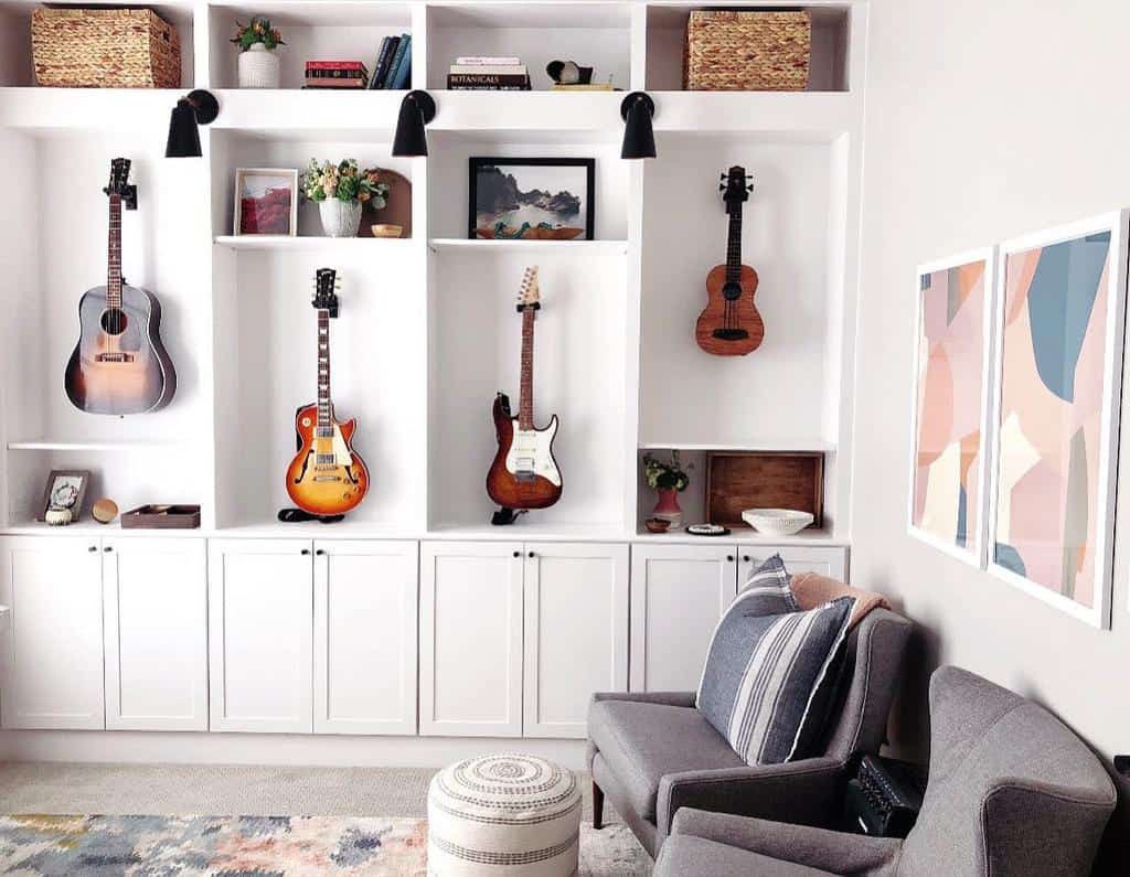 Stylish music room with wall-mounted guitars, built-in white shelving, cozy seating, soft pastel decor, and modern lighting