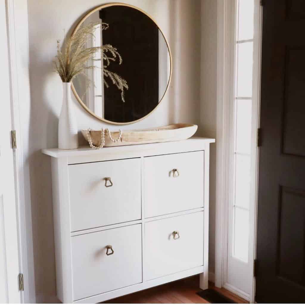 Minimalist entryway with a white storage cabinet, round mirror, neutral decor, and soft natural lighting for a modern, inviting look