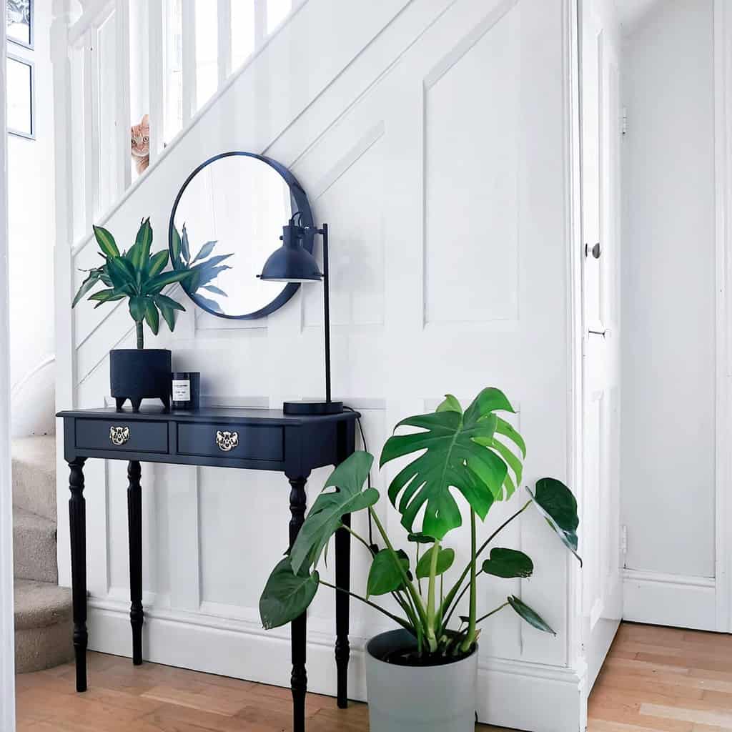 Modern entryway with a black console table, round mirror, potted greenery, and a sleek black lamp for a stylish monochrome look