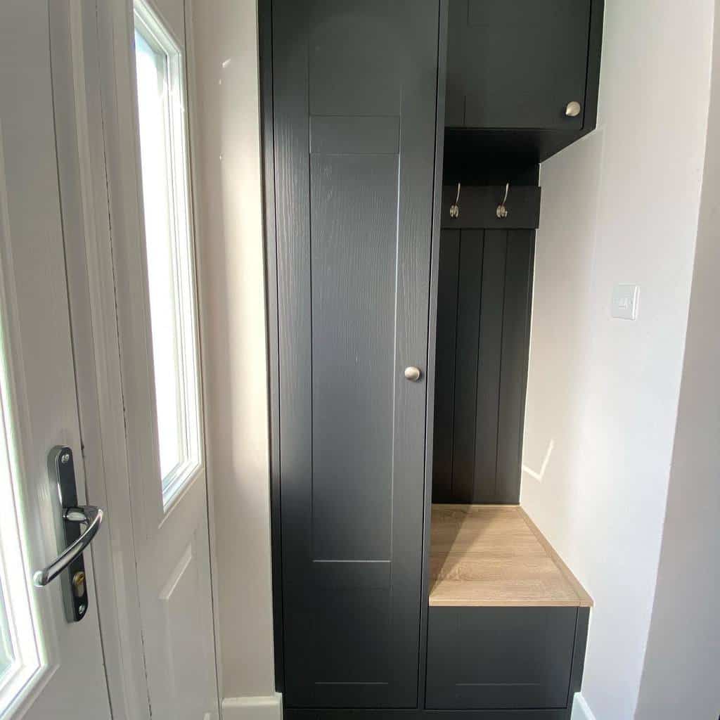 Compact modern entryway with built-in dark cabinetry, a wooden bench, and coat hooks for a sleek and functional storage solution