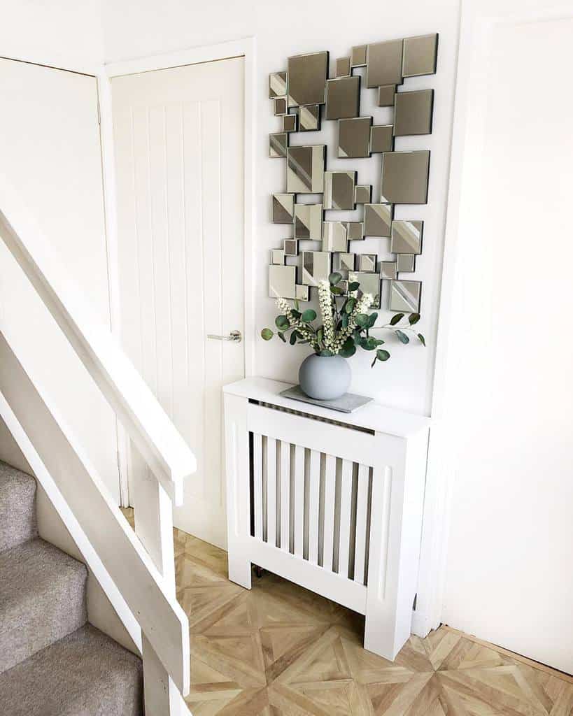 Modern entryway with a geometric mirror wall, sleek white radiator cover, neutral decor, and a touch of greenery for a fresh look