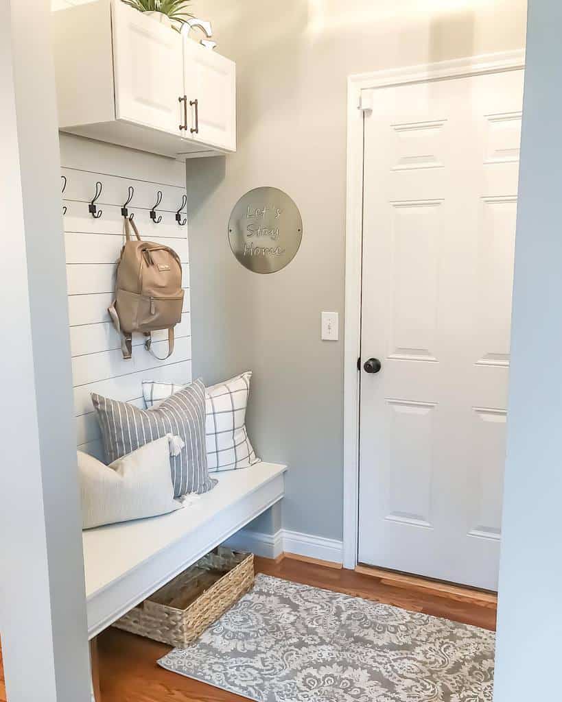 Cozy modern entryway with a built-in bench, shiplap wall, overhead storage, hooks for organization, and soft neutral decor