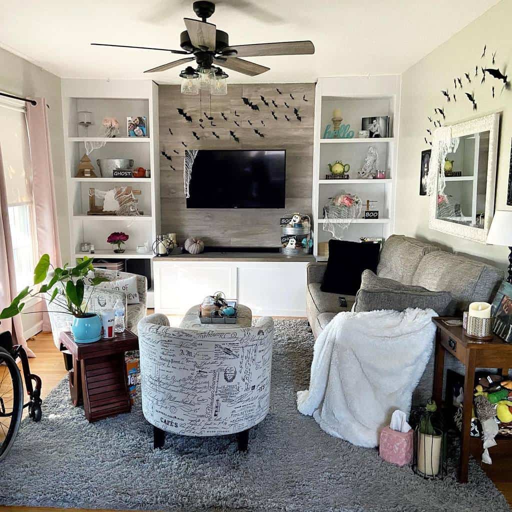 Small living room with a TV, gray sofa, patterned chair, ceiling fan, and decorative shelves featuring plants and various ornaments.