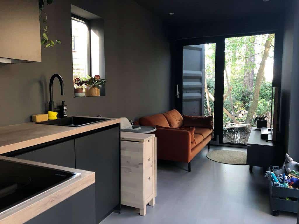 Modern tiny home with sleek black cabinetry, a warm-toned sofa, and large glass doors opening to nature. Minimalist and cozy design.