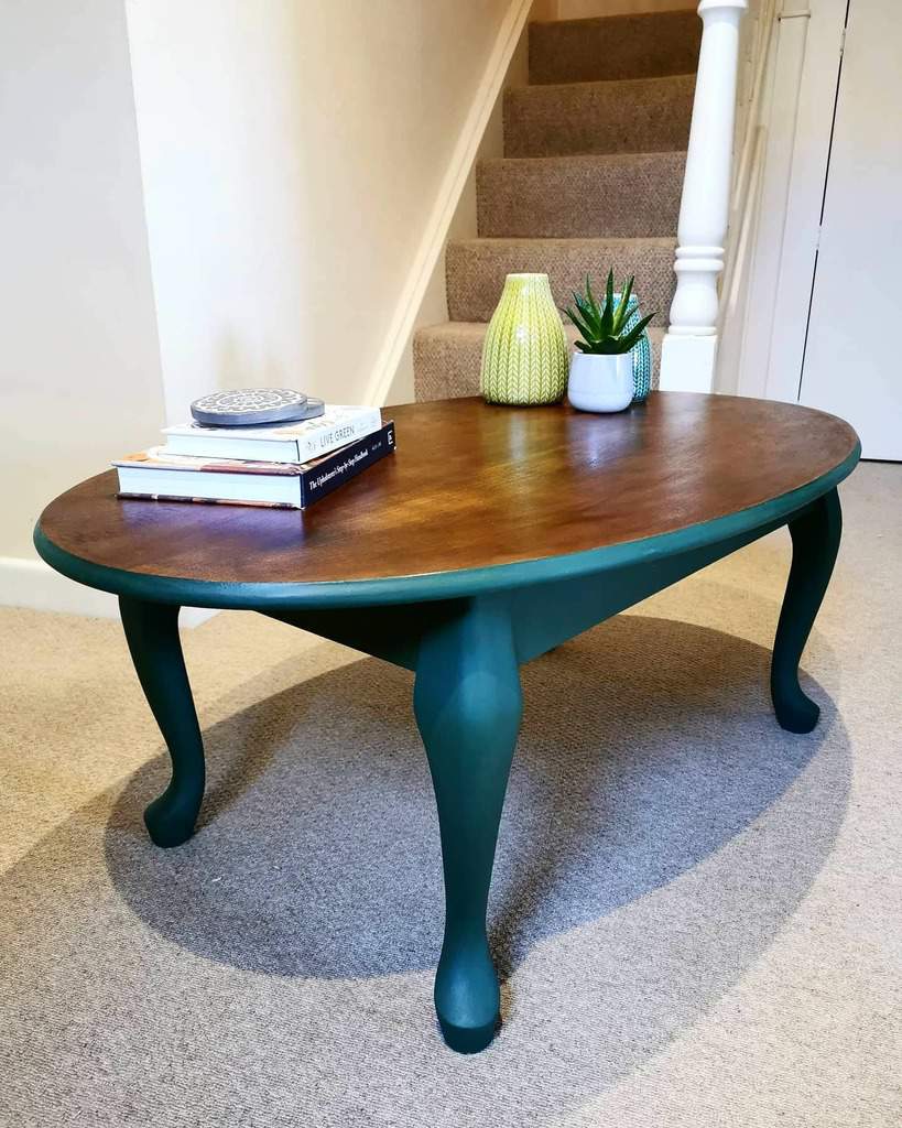 Oval coffee table with a wooden top and green legs, placed on a light carpet, decorated with books and vases