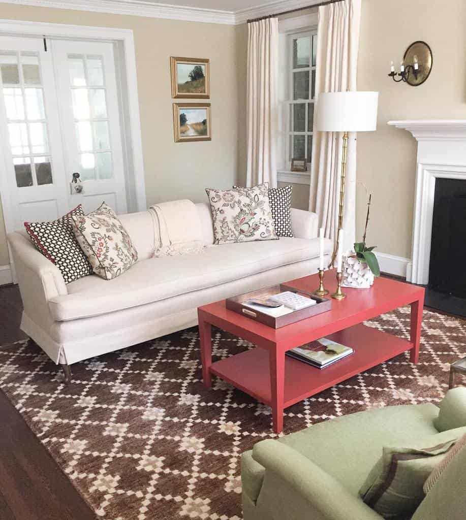 Stylish living room with a white sofa, patterned pillows, a red coffee table, green chair, and a geometric rug enhanced by wall art and lamps for added decor