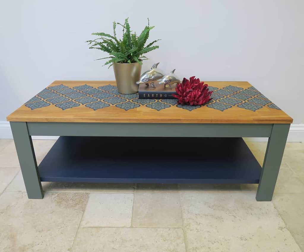 Wooden coffee table with geometric tile pattern, metallic dolphins, a potted fern, and a red flower on a beige tiled floor