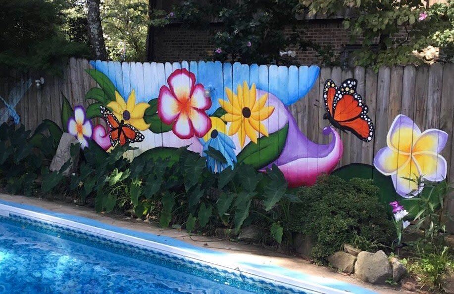 Colorful hand-painted pallet fence with vibrant flowers and butterflies, creating a lively and artistic backdrop for a poolside garden