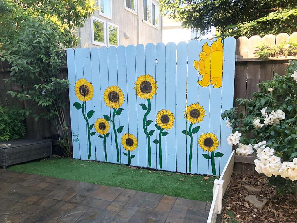 Light blue wooden fence painted with bright yellow sunflowers and a cheerful sun, adding a whimsical touch to the backyard space