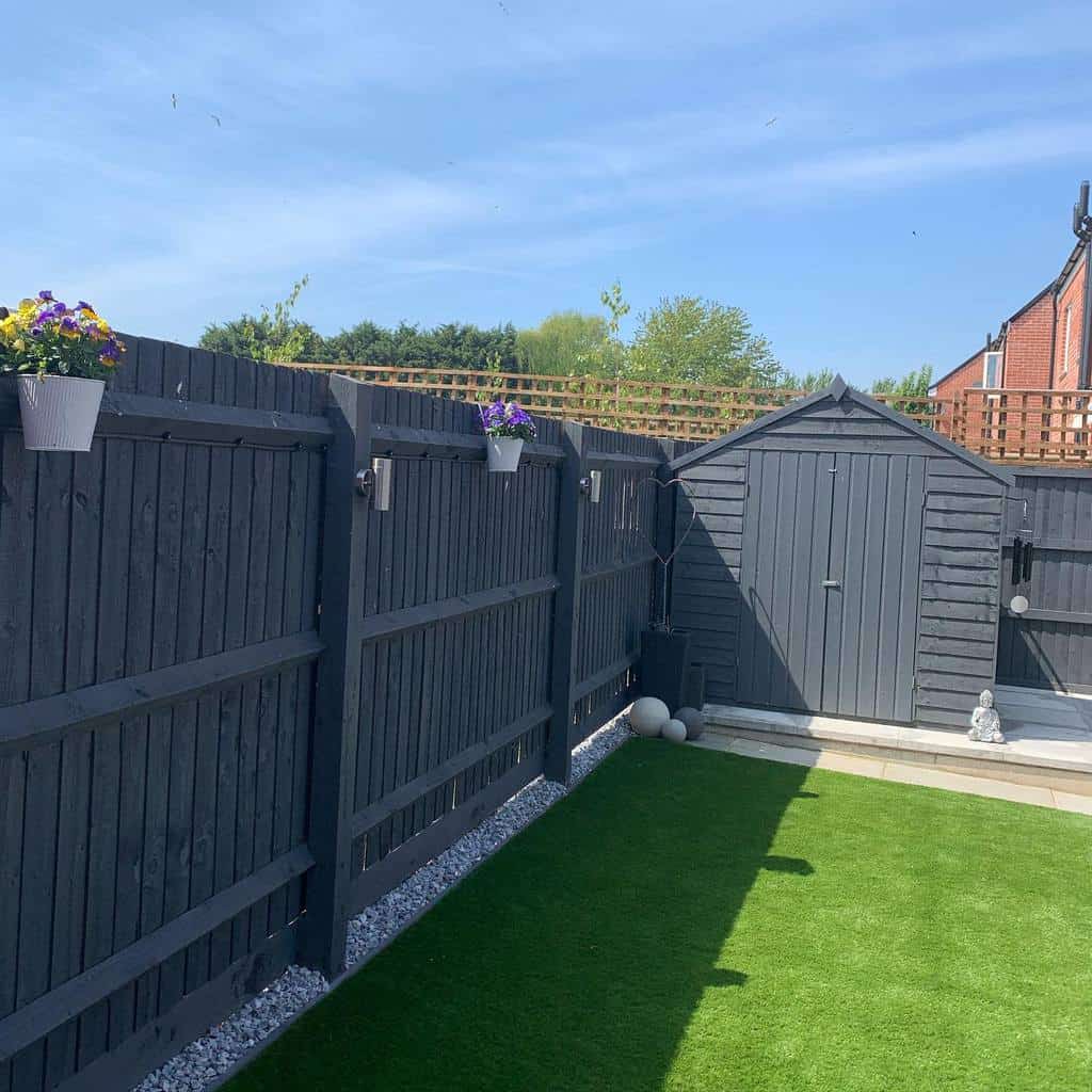 Stylish dark grey wooden fence with matching shed, accented by hanging flower pots and outdoor lighting, creating a modern backyard retreat