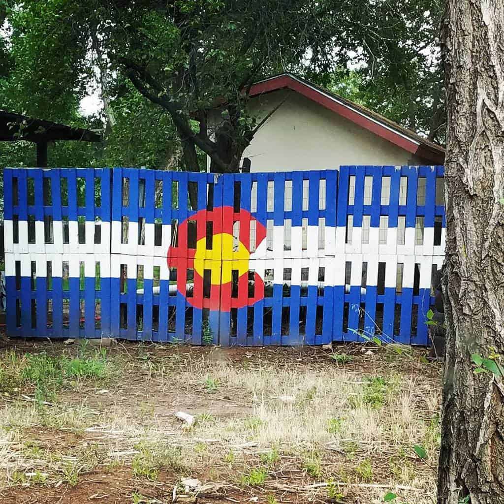 DIY pallet fence painted with the Colorado state flag, featuring bold blue, white, red, and yellow colors for a rustic patriotic display