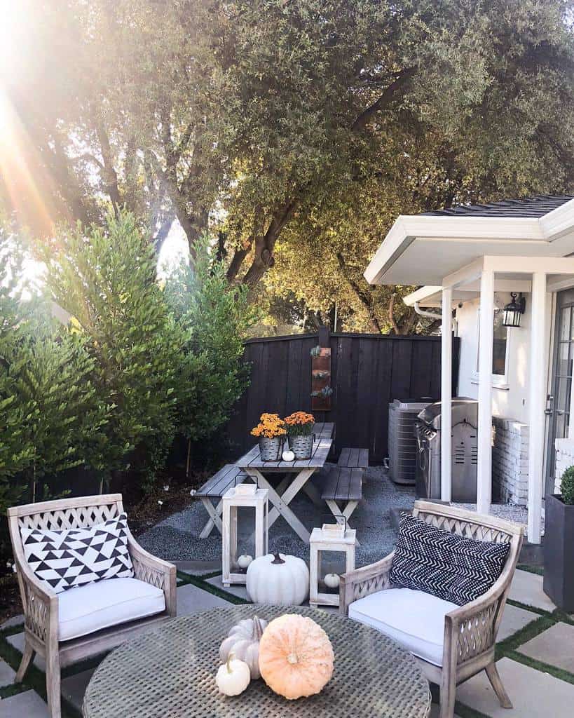 Side yard patio with wooden chairs, a round table, fall-themed decor, a picnic table, string lights, and lush greenery under large trees