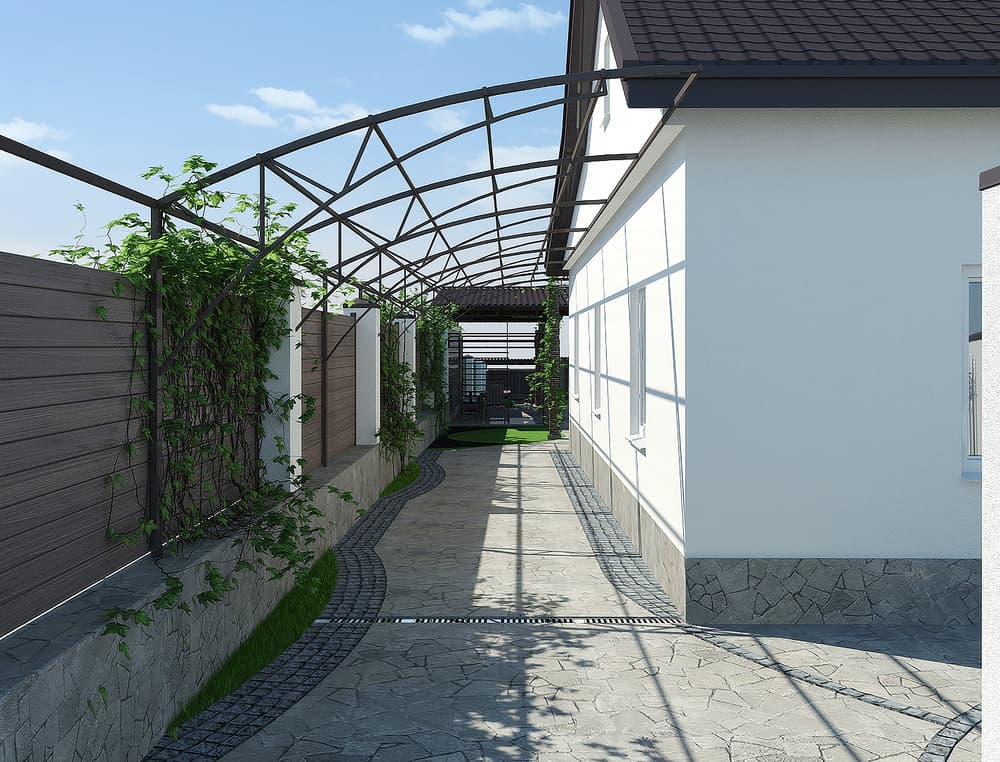 A stone walkway beside a white house is covered by a metal trellis with climbing plants