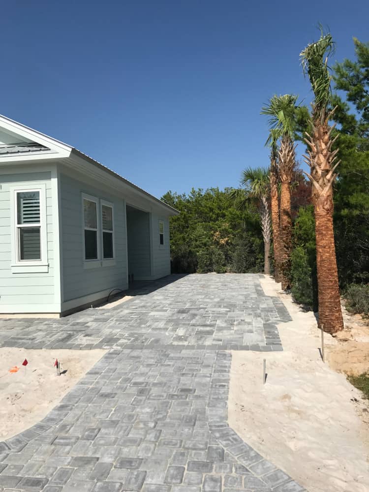 Pathway with gray pavers leads to a pale blue house surrounded by palm trees