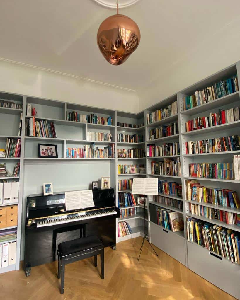 Elegant music library with a black upright piano, floor-to-ceiling bookshelves, a copper pendant light, and a warm wooden floor