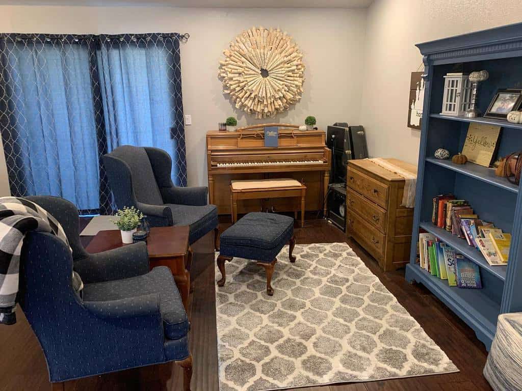 Cozy music room with a wooden upright piano, navy blue seating, a patterned rug, a blue bookshelf, and warm decorative accents