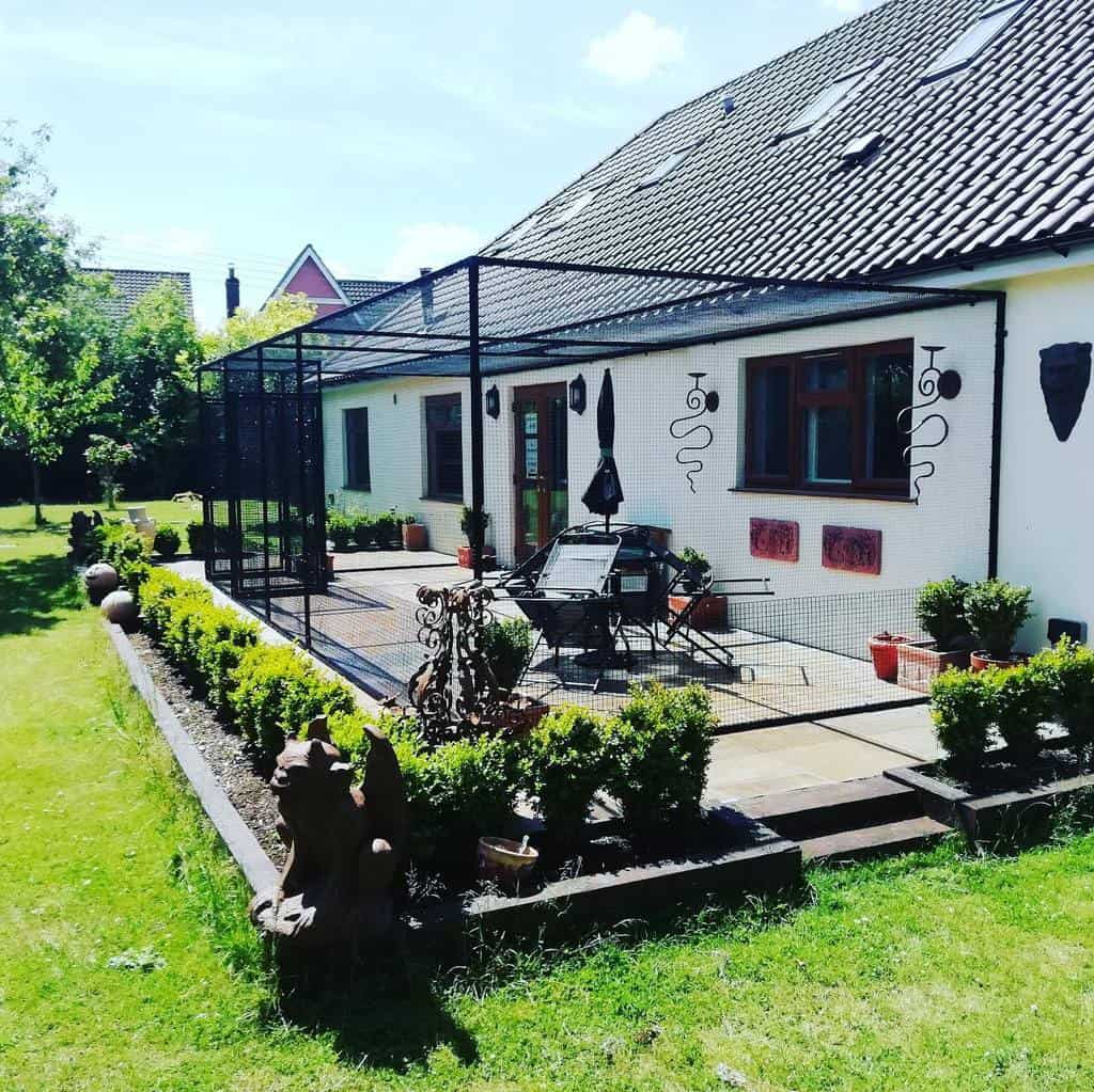 Spacious porch catio with a black mesh enclosure, attached to a modern house, providing a safe outdoor space for cats and relaxation