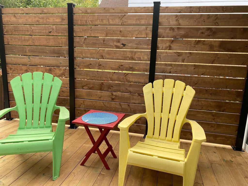 Modern horizontal wooden privacy fence with black metal posts, creating a cozy and stylish backyard deck with colorful Adirondack chairs