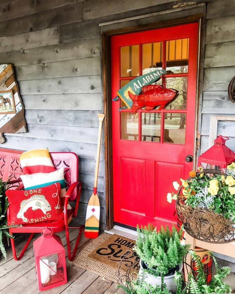 Cozy porch with a bright red door, "Alabama" sign, fishing-themed decor, plants, and red lanterns on rustic wood siding