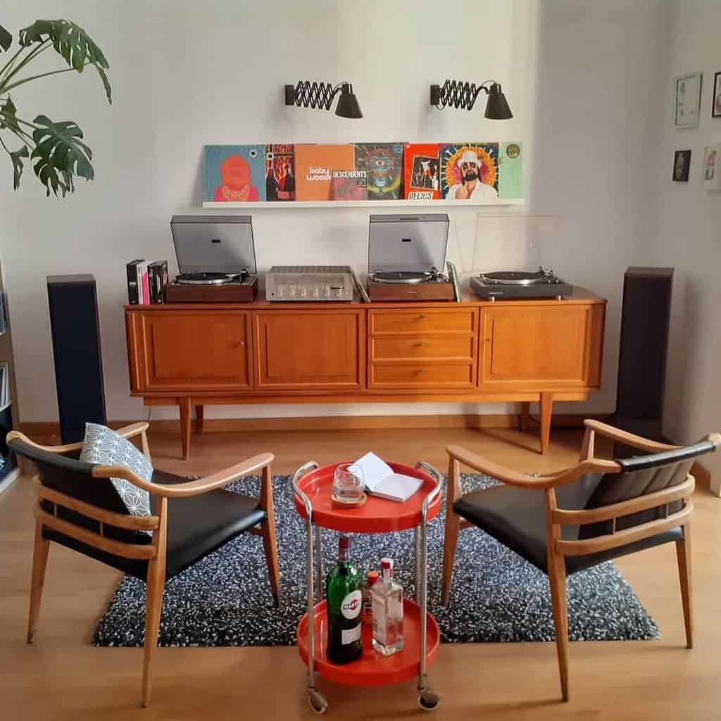 Stylish retro music room with turntables, a vintage wooden console, vinyl records, mid-century chairs, and a chic red bar cart