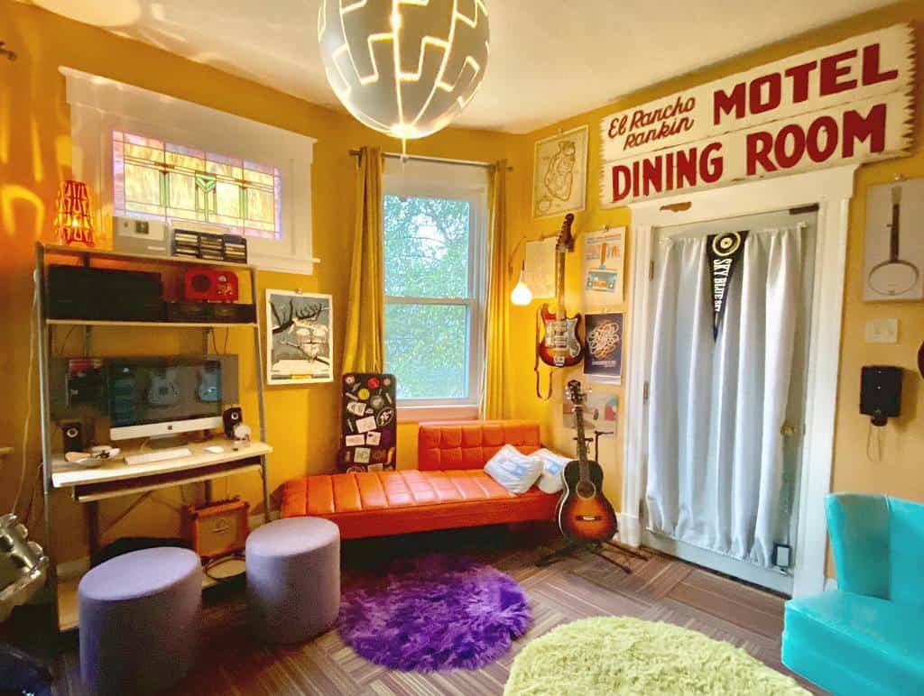 Vibrant retro music room with colorful decor, wall-mounted guitars, a cozy orange sofa, a workstation, vintage signs, and eclectic lighting