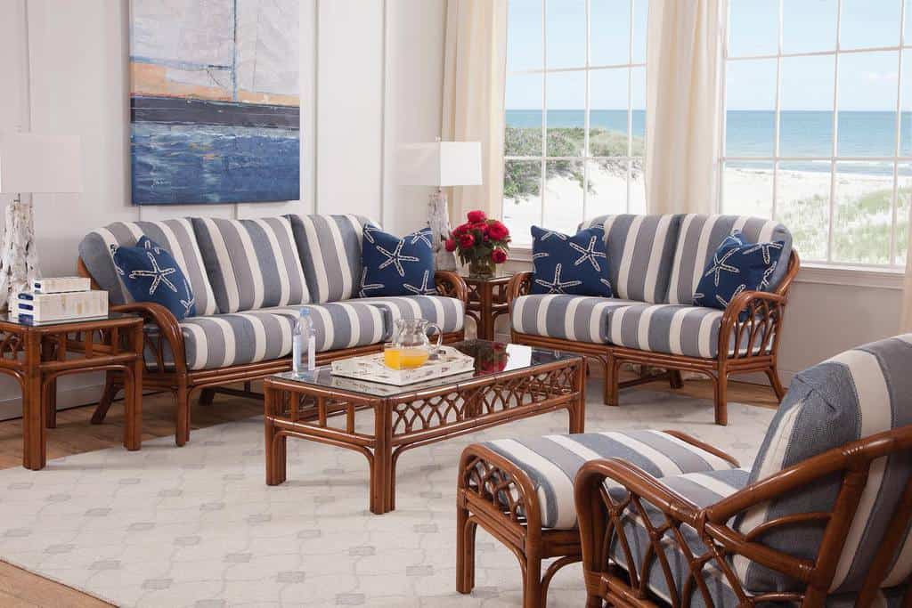 A beach-themed living room with striped furniture, nautical pillows, a glass coffee table, large windows, and an ocean view