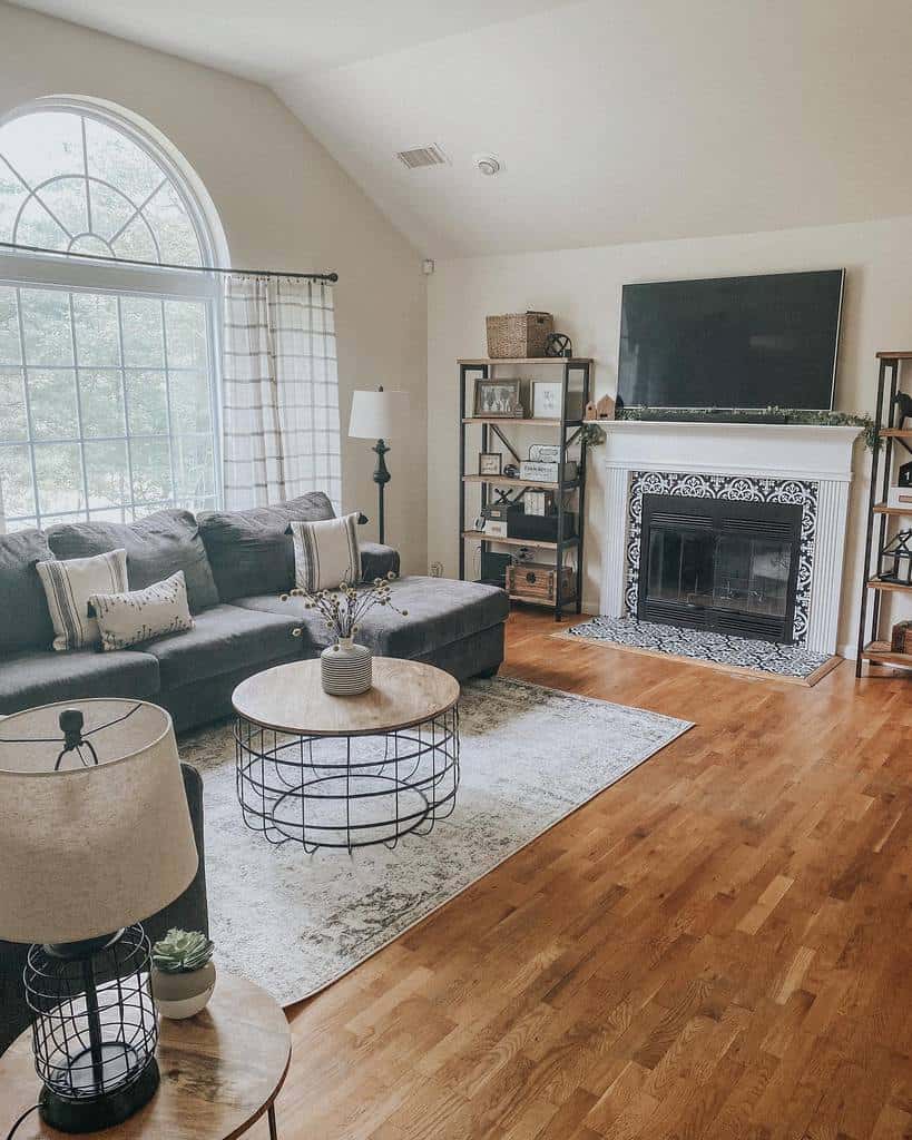 Round rustic coffee table with a wooden top and metal wire base, styled with a vase, set in a cozy living room with a fireplace