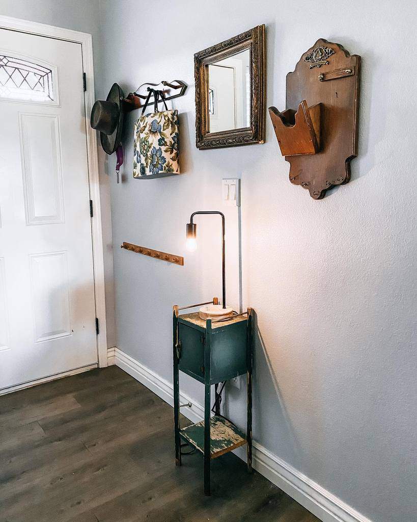 Rustic entryway with vintage wall decor, a distressed wooden side table, antique mirror, and wall hooks for stylish organization