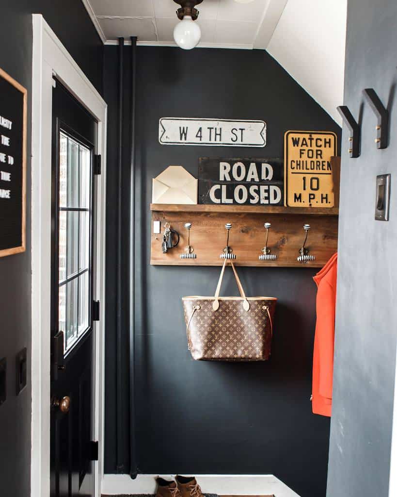 Industrial-style entryway with dark walls, vintage road signs, a wooden coat rack with hooks, and a bold mix of rustic and urban decor