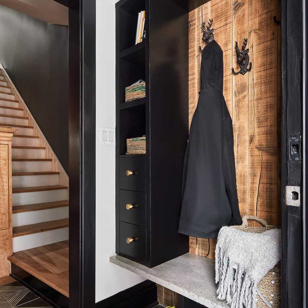 Rustic-modern entryway with black built-in storage, wood-paneled coat hooks, brass accents, and a concrete bench for a sleek yet cozy look