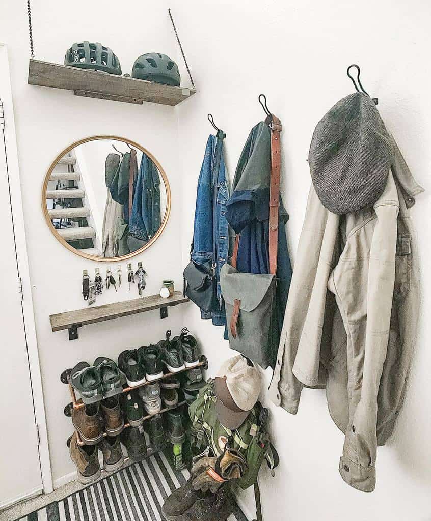 Compact and functional entryway with wall hooks, a round mirror, floating shelves, vertical shoe storage, and rustic decor for an organized space