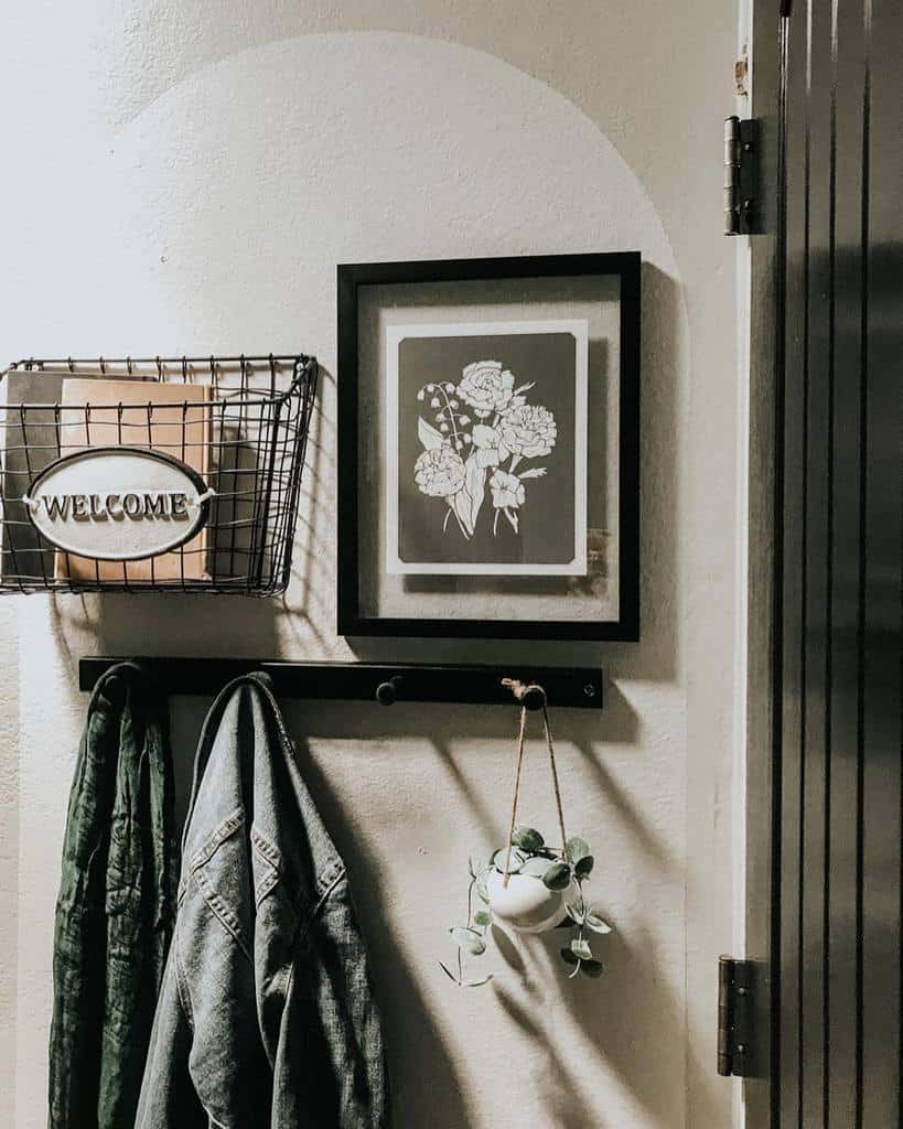 Cozy rustic entryway with a wire basket organizer, black wall hooks, framed floral artwork, and a small hanging plant for a warm touch