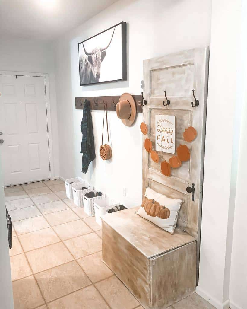 Rustic farmhouse entryway with a repurposed door bench, seasonal fall decor, wall hooks for organization, and a Highland cow print